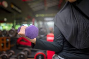 Arab middle eastern muslim woman working out while lifting a dumbbell at the gym. Fitness exercise and healthy lifestyle concept
