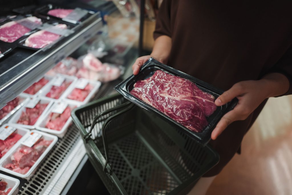 Woman holding a tray filled with fresh red meat while browsing the supermarket, carefully selecting ingredients for dinner